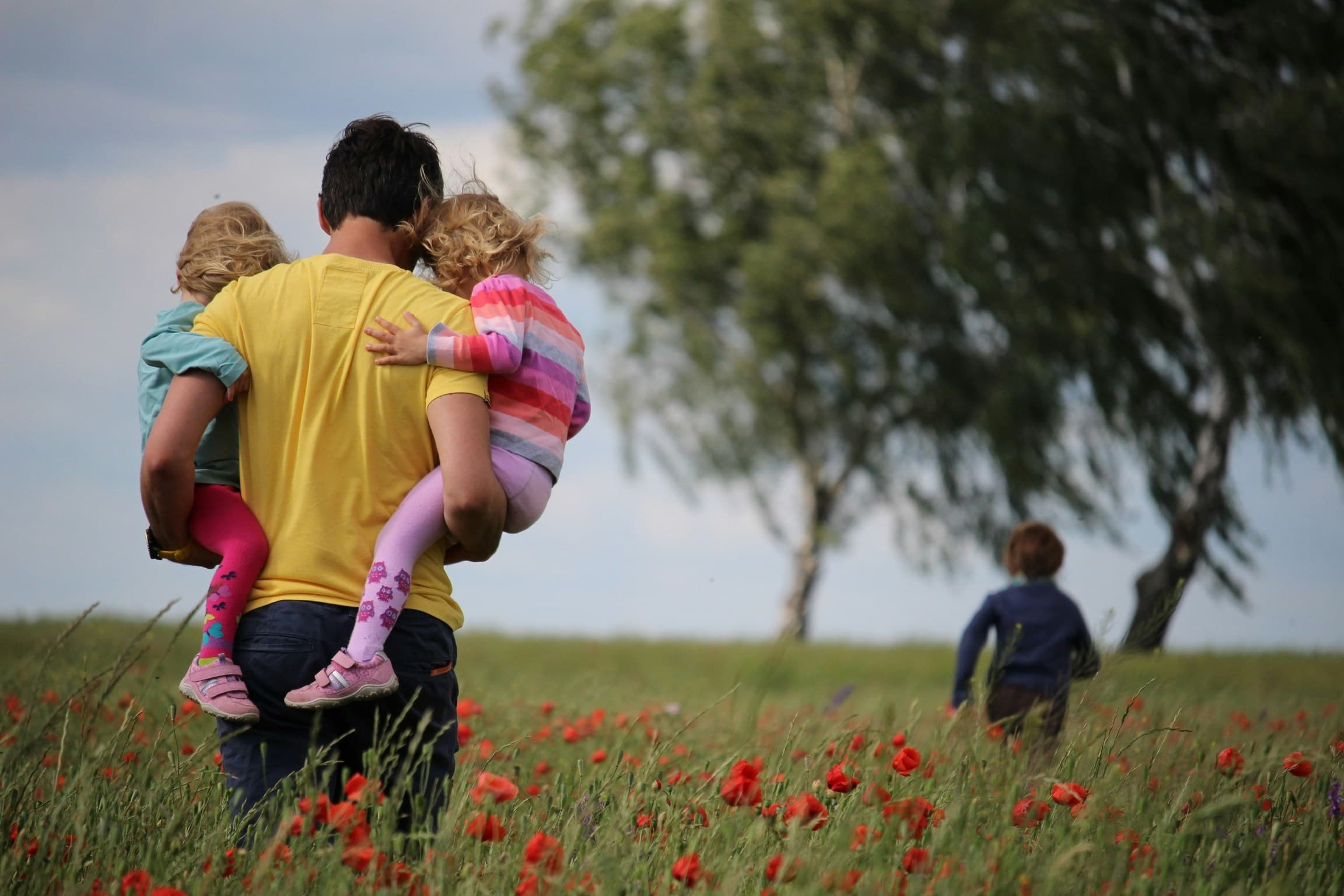 A parent carrying two children through a field
